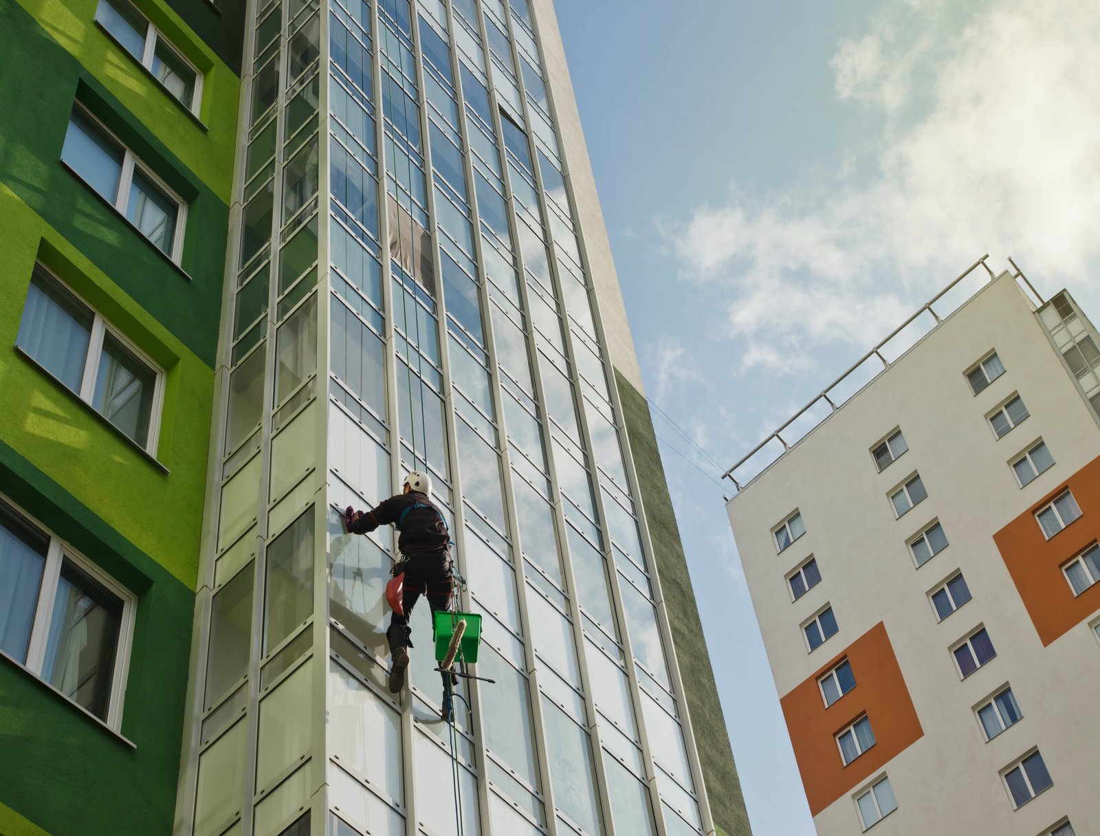 Industrial mountaineering worker hangs over residential building while washing exterior facade glazing. Rope access laborer hangs on wall of house. Concept of urban works. Copy space