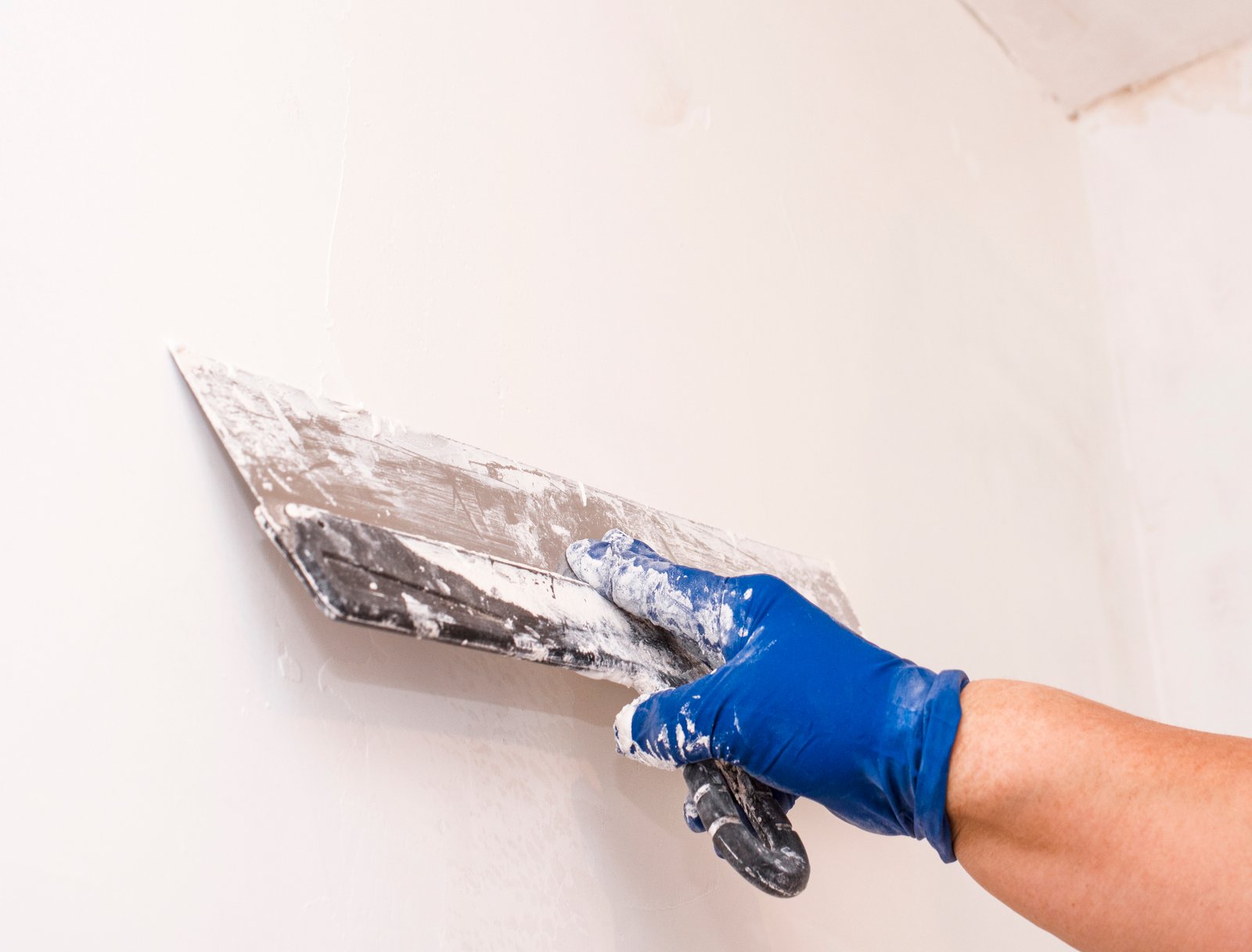 Using a spatula align the wall. A blue-gloved hand. Interior decoration.