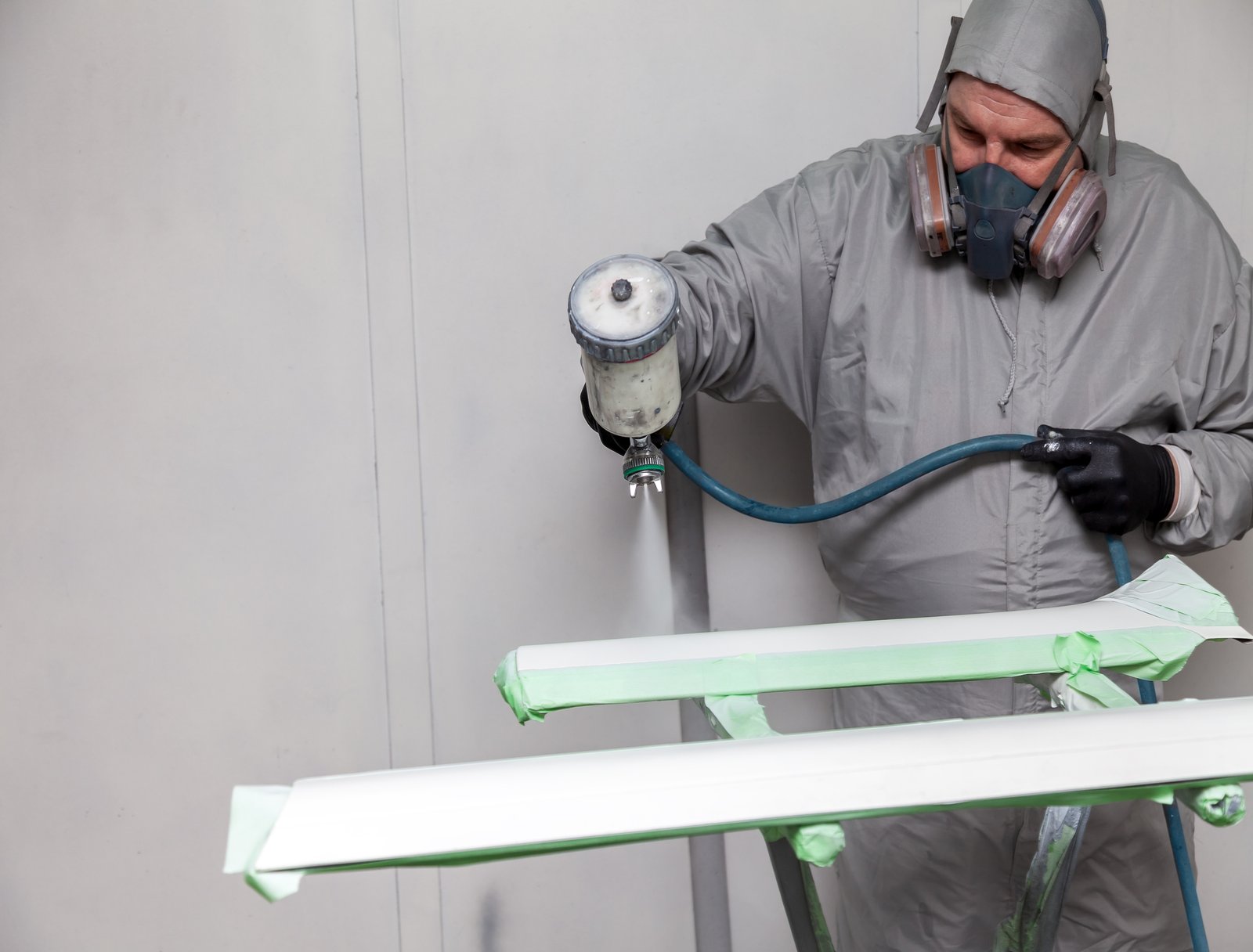 A male worker paints with a spray gun a part of the car body in silver after being damaged at an accident. Plastic elements from the vehicle during the repair in the workshop auto service.