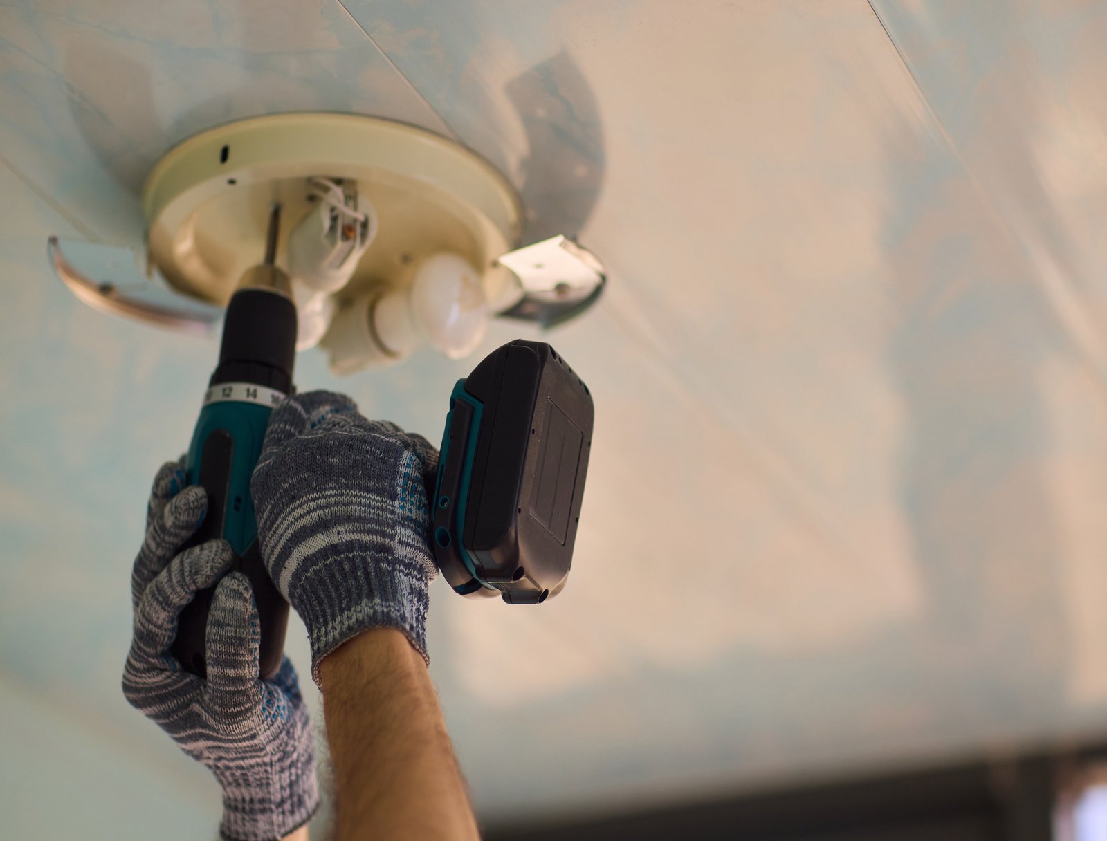 A skilled man expertly uses a powerful electric drill to install a modern ceiling light, showcasing his DIY talents