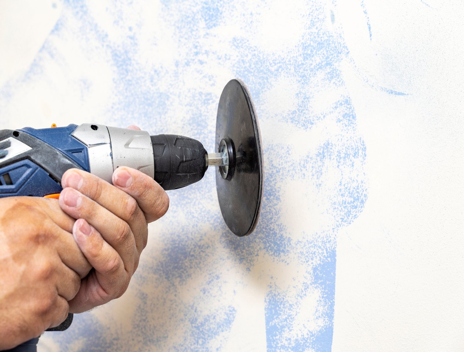The plasterer levels the surface of the wall with a sander. the master removes the old paint from the surface. Copy space.