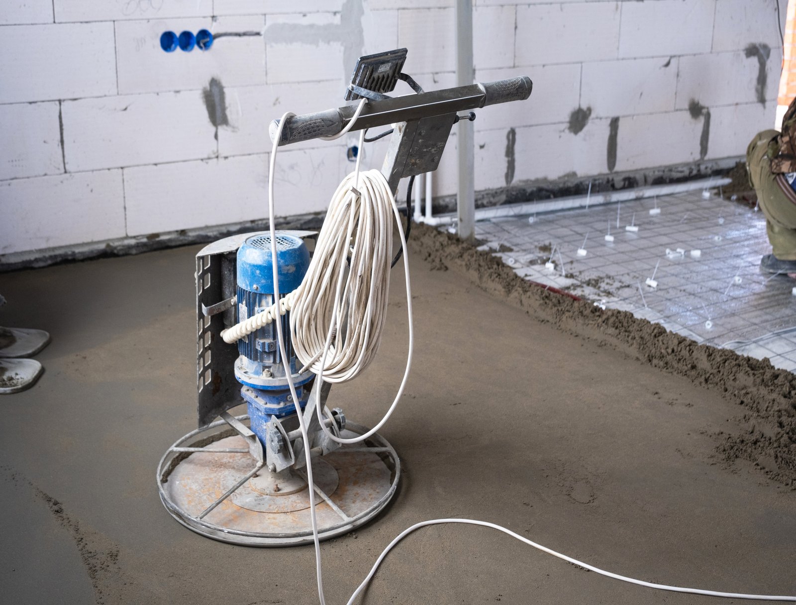 Ramming and grinding of semi-dry floor screed by a machine with a rotating disk for leveling. Construction of a concrete floor in the house, a master with special equipment.