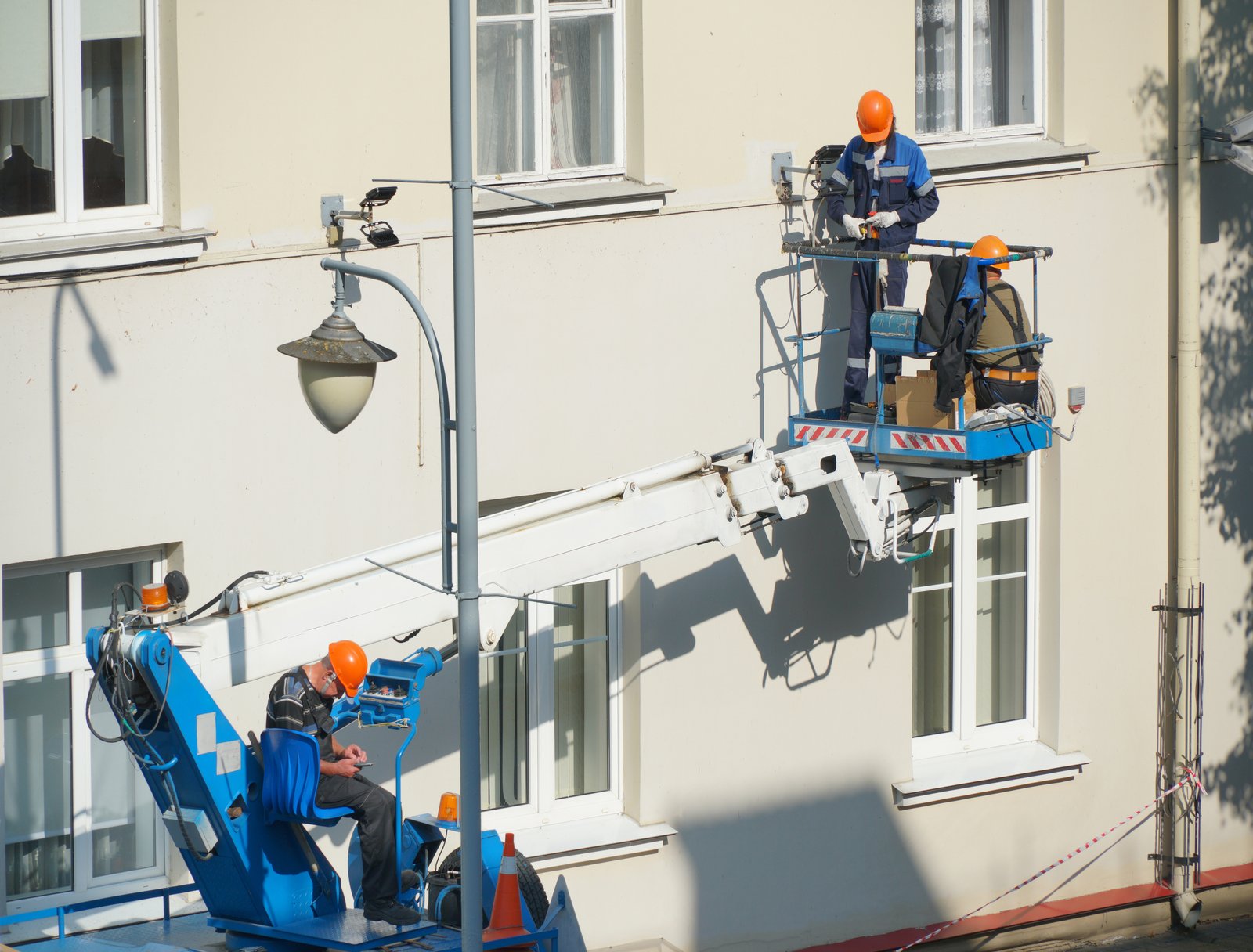 A worker in the bucket of a crane is installing lighting on the facade of the building. Renovation of the facade of the building, installation of lighting equipment, urban illumination.