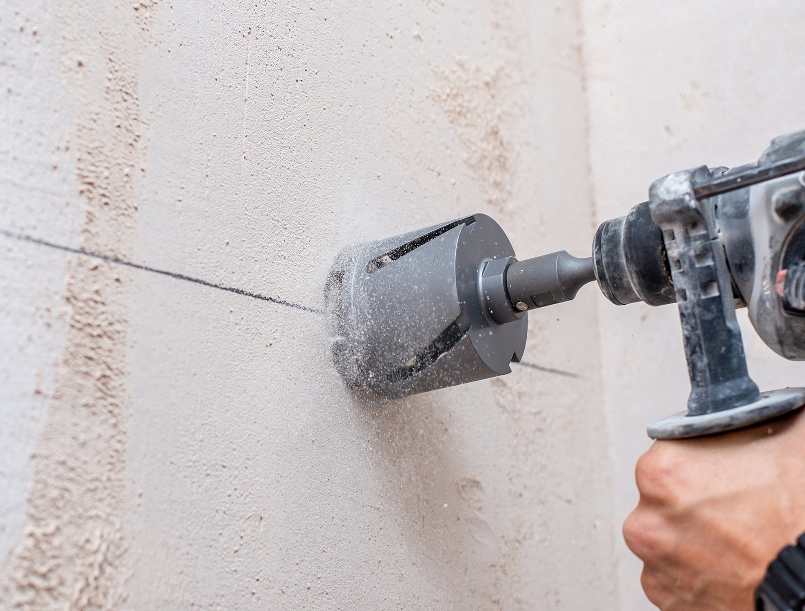 working drill with a special drill for holes for the output of wires in men's hands against the background of a peach wall
